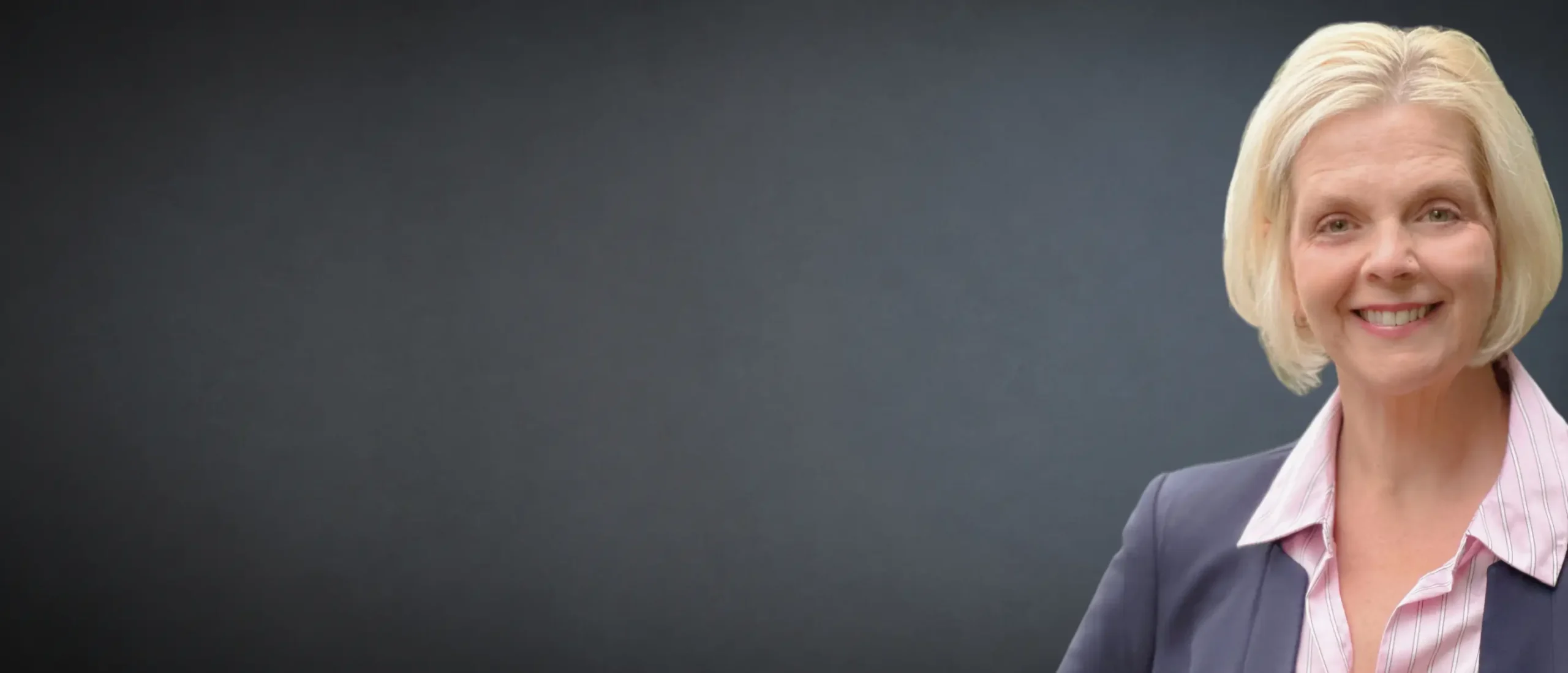 Professional portrait of a smiling executive in business attire standing against a dark background.